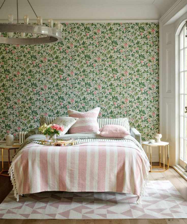 A bedroom with a green floral wallpaper accent wall, and a bed with pink striped bedding.