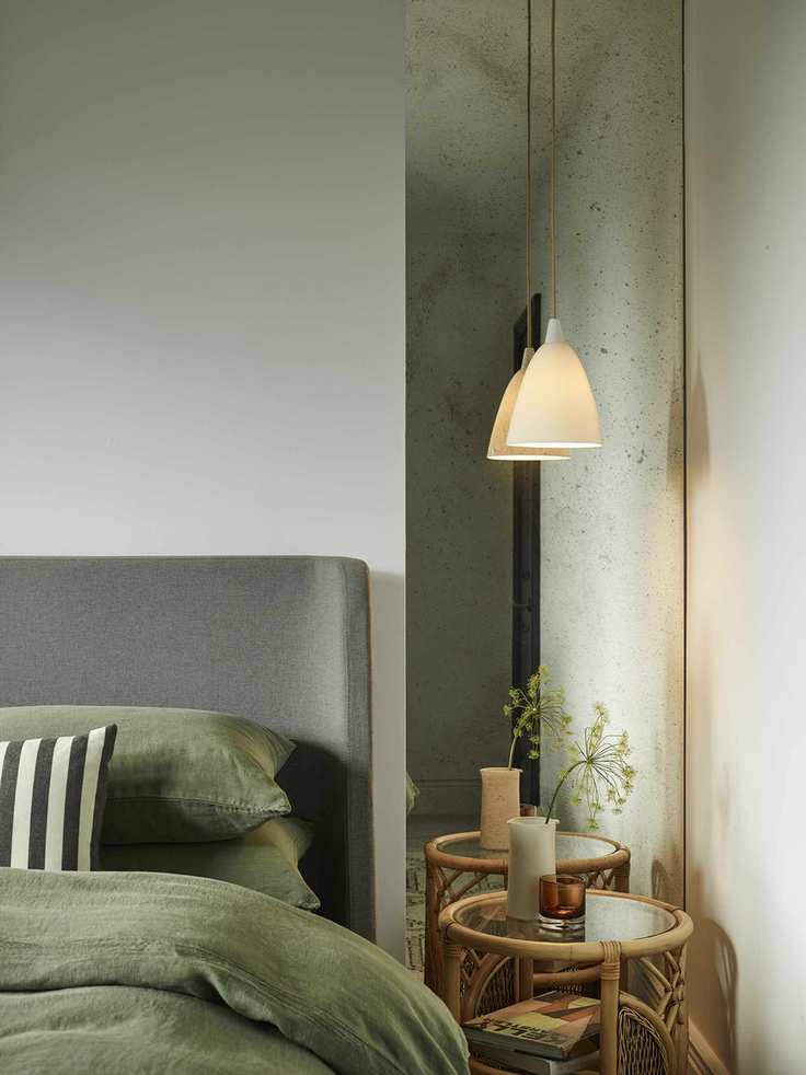 green bedroom with pendant light hanging in front of mirror, rattan side table, green bedding, green bed, pale green painted walls