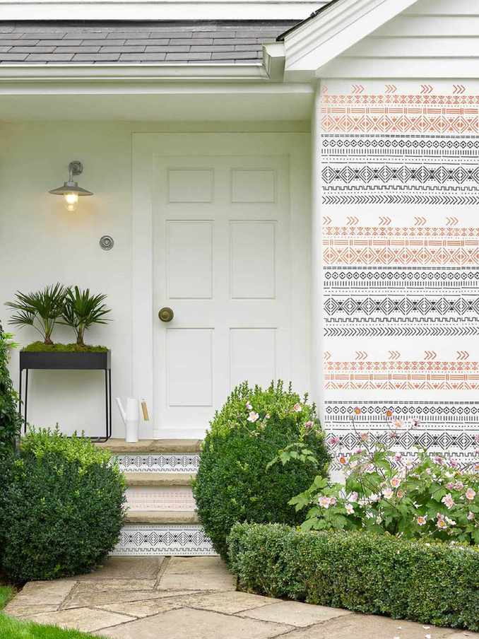 front porch with painted pattern on steps and cladding as well as neatly trimmed evergreen low-profile shrubs and pink flowers