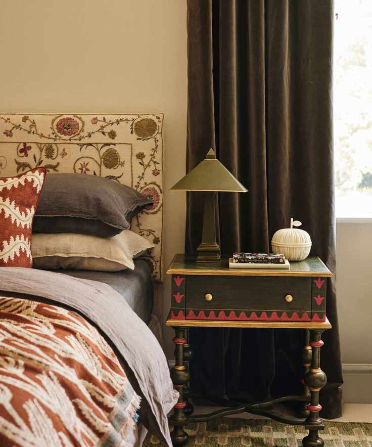 A serene bedroom featuring a patterned headboard and a painted side table.