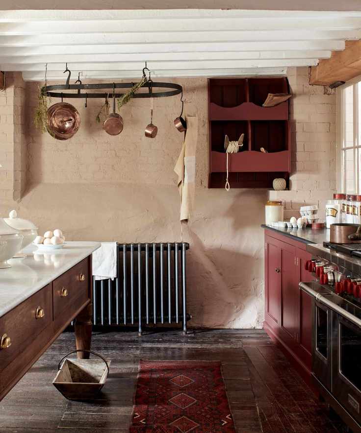 A country kitchen with deep pink cabinets, a wooden freestanding island, and a wall-mounted veg box for storage