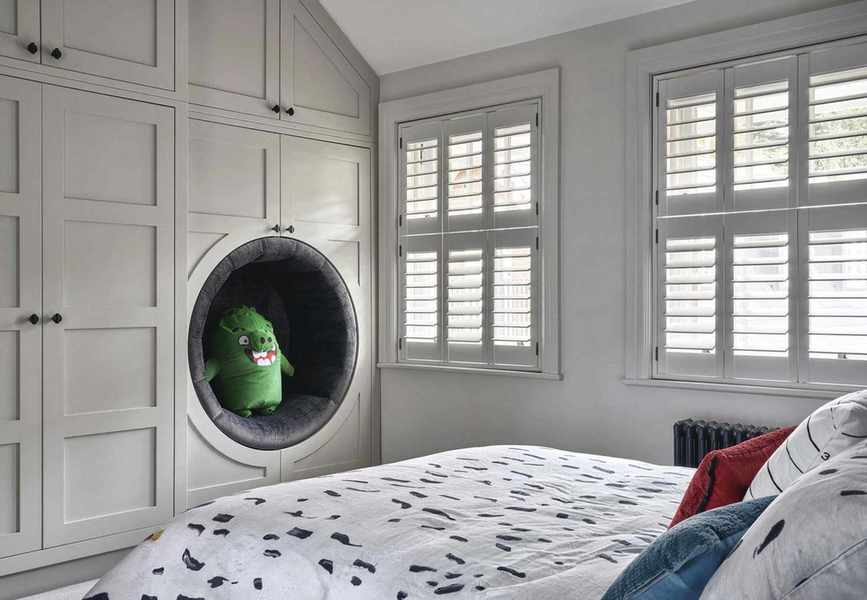 Child's bedroom with bed with patterned linen, built in wardrobes and reading nook and shutters on windows