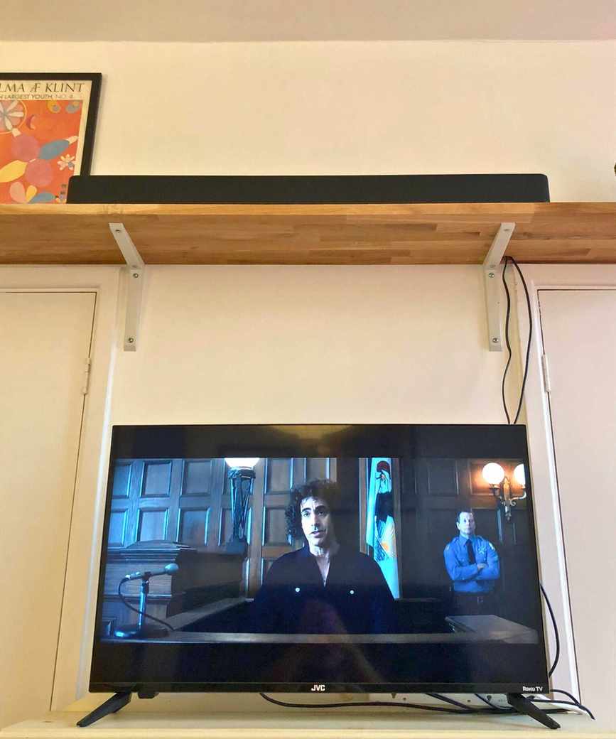 TV displaying Trial of the Chicago 7 with the Fire TV Soundbar Plus on a wooden shelf.