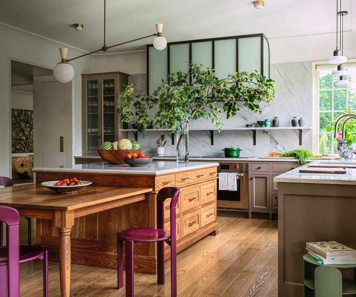 Brown kitchen with wooden island, white worktops and wooden dining table with pink chairs
