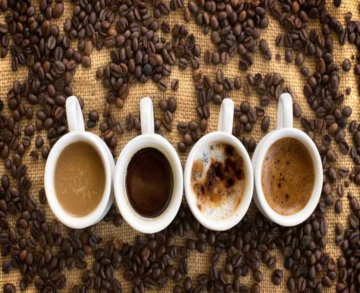 Four cups of coffee beans on hessian with beans scattered around them