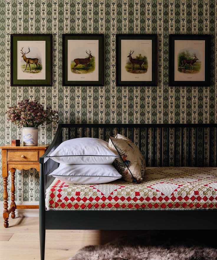 a wallpapered bedroom with a day bed, patchwork blankets and vintage deer artwork
