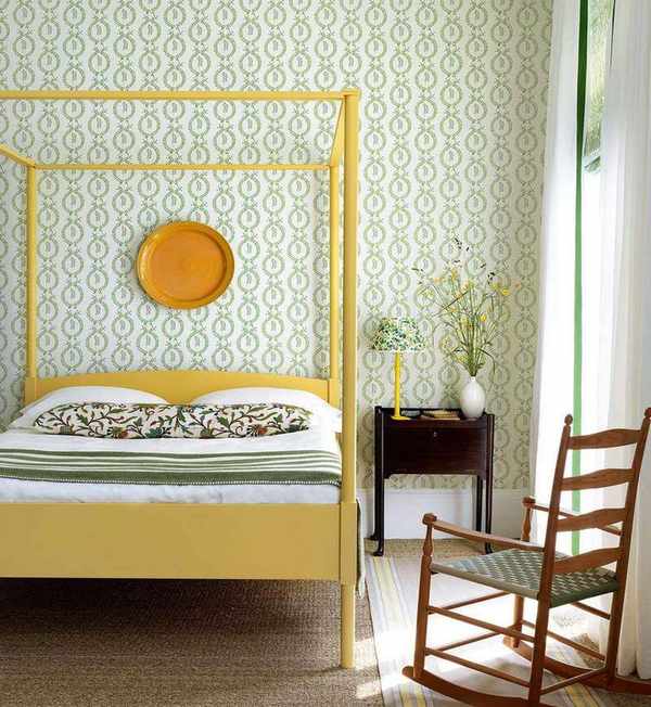 A yellow four-poster bed in front of a wall with green and white patterned wallpaper