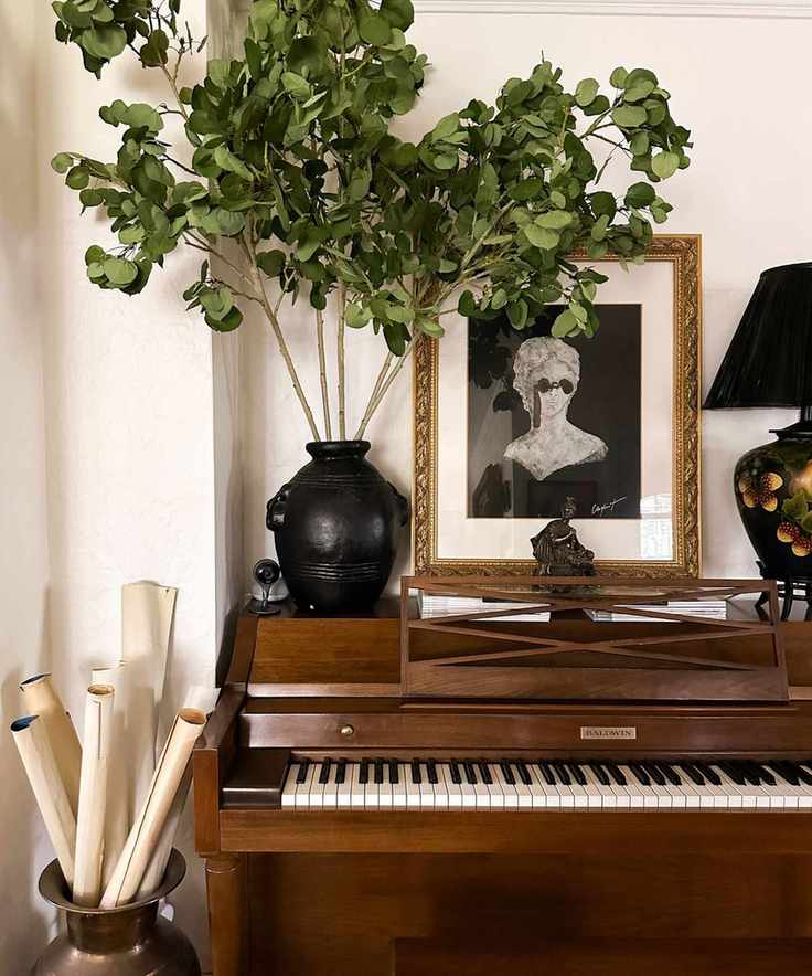 Piano with old framed portrait, lamp, rustic vase with foliage and vase with maps