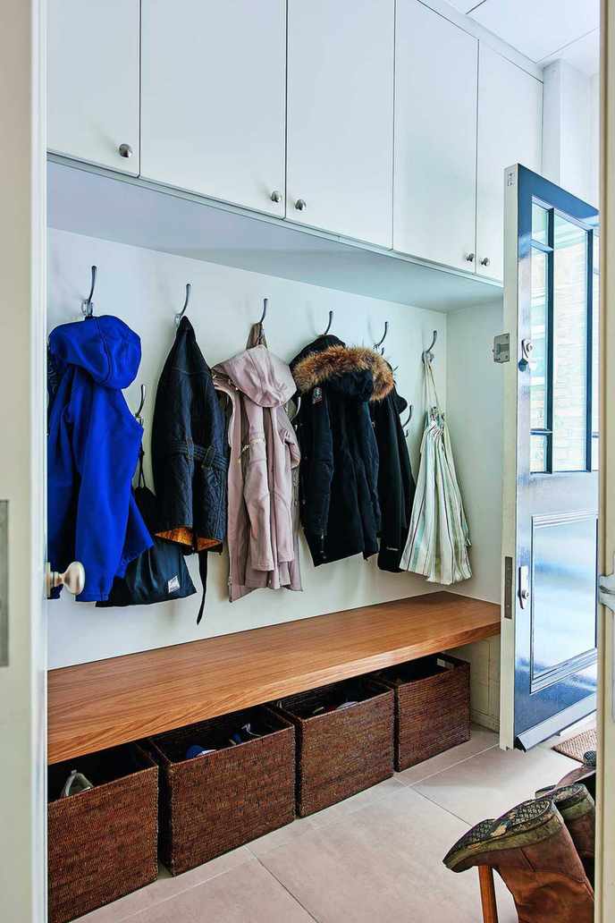 Entryway with stone floor, coats on hooks with bench and baskets below, and cabinets above