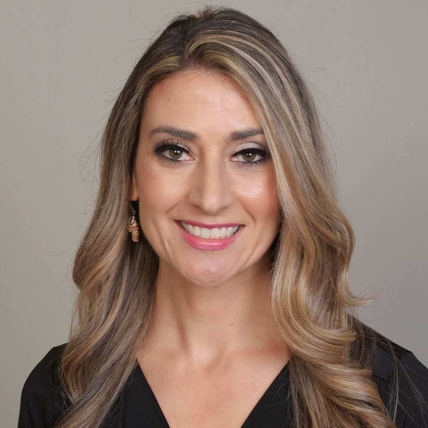 A headshot of Diane Delaney - a woman wearing a black dress and gold earrings, with a grey background behind her
