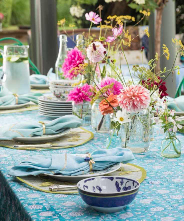 Table setting in light blues and greens with pink flowers in glass jars along the center