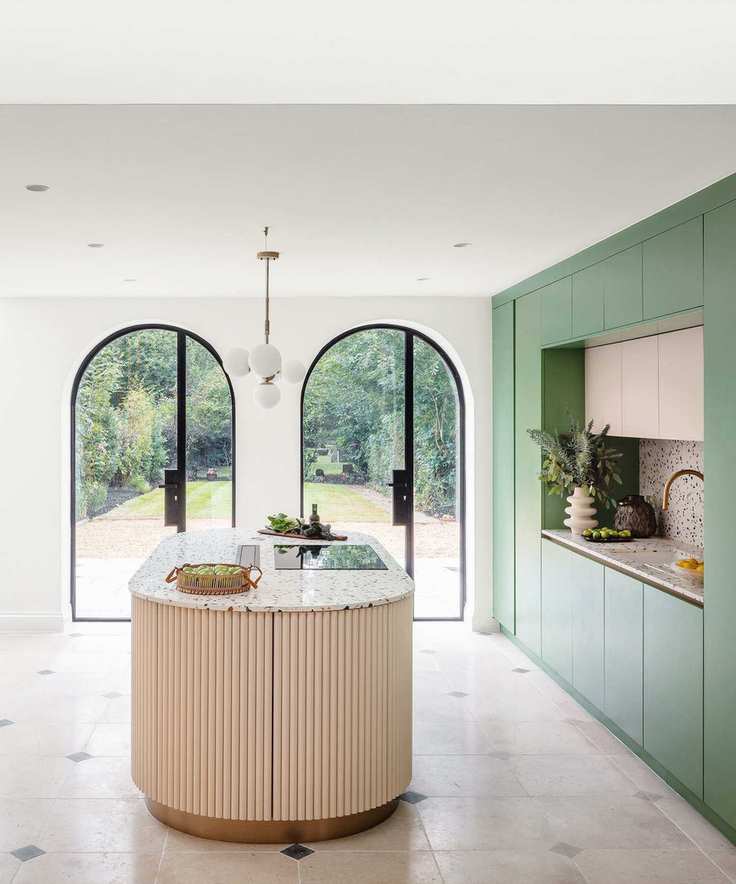Bright modern kitchen with two arch windows, large oval island, blue cabinetry, tiled flooring