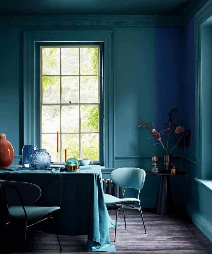A striking teal dining room featuring walls and ceiling in teal, matching table cloth, dark wood flooring, and decorative elements