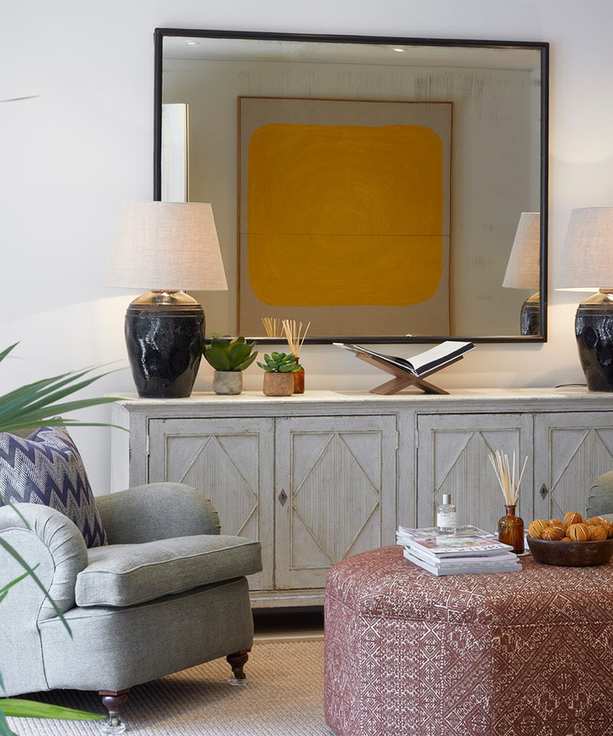 Ideas to decorate small spaces in a neutral living room scheme with large mirror, whitewashed wood sideboard, taupe sofa and red patterned footstool.