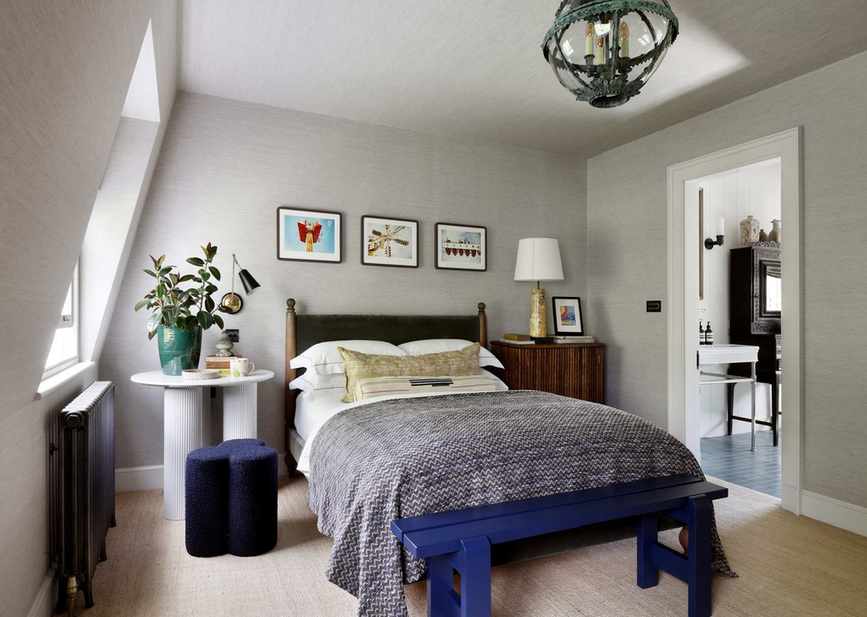 A bedroom with gray grasscloth wallpapered walls, a wooden bed frame, and a large white nightstand