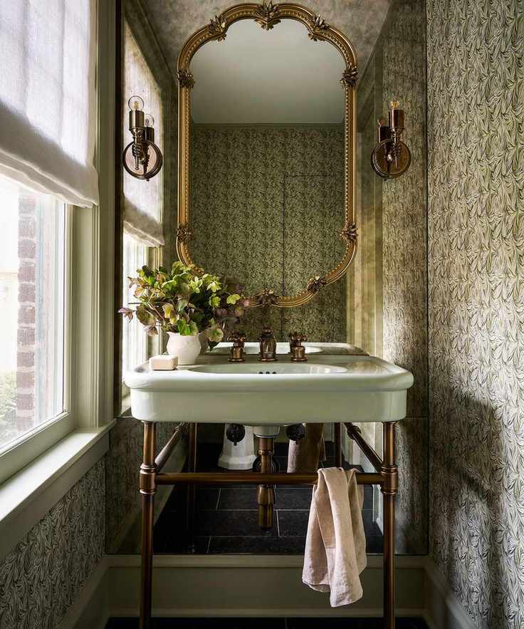 Small bathroom with muted green wallpaper and brass fixtures.