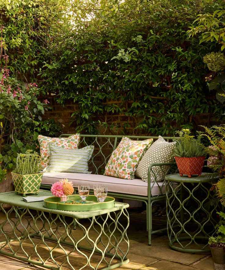 green trellis style rattan outdoor furniture on a small walled garden patio with floral pillows and a coffee table styled with a potted plant and drinks tray