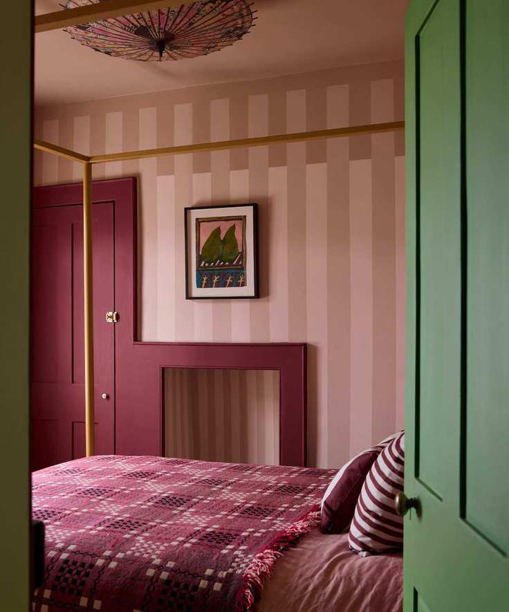 A bedroom with thick pink striped wallpaper, red and pink bedding, a dark red door and woodwork, and a dark green paint used on the door leading into the room.