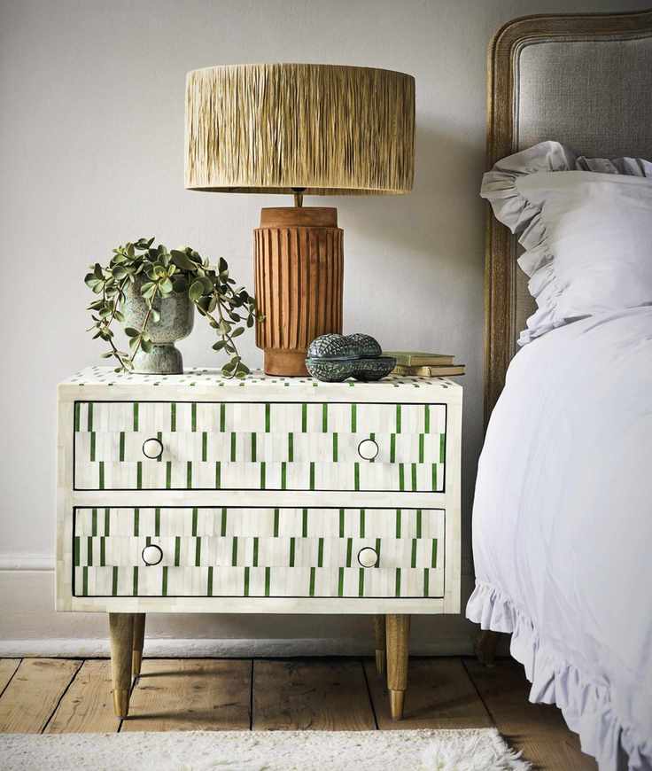 bedroom with bone inlay nightstand in green and cream, upholstered bed with check blanket, gold table lamp, plant, wooden floor