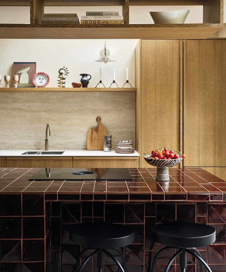a wooden galley kitchen with a burgundy tiled kitchen island with black stools