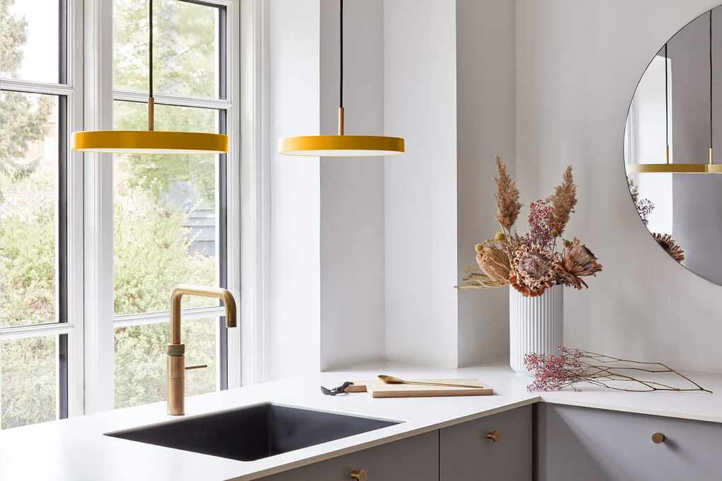 modern yellow pendant lights over a basin with brass tap, white countertop