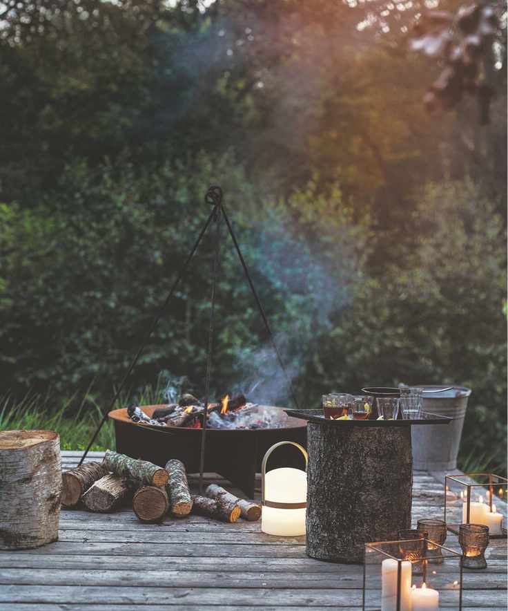 A decking with a firepit and candles with leafy greenery in the background