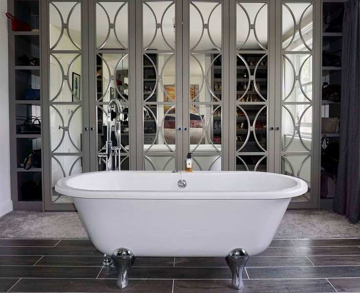Rolltop white bath in bedroom with large wardrobe with mirrored doors, mix of carpet and wooden flooring