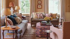 an English country living room with a woven rug, two neutral couches, patterned pillows, patterned otoman and a pattern armchair
