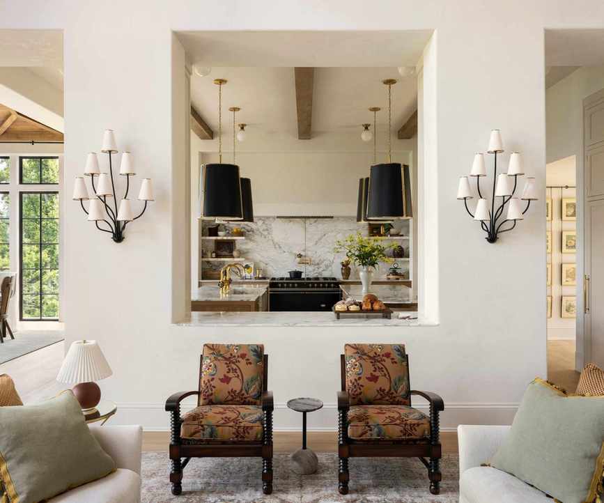 A warm white living room with a large pass-through window into a wood and marble kitchen