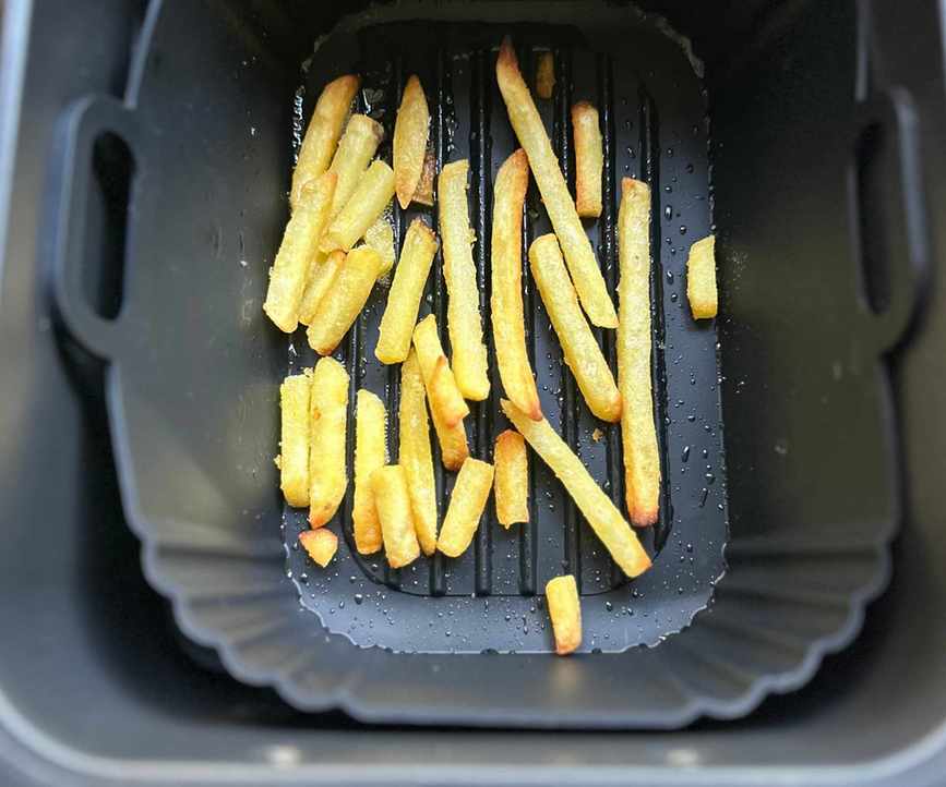 A black silicone air fryer liner with a few fries in the base, inside a black air fryer basket drawer.