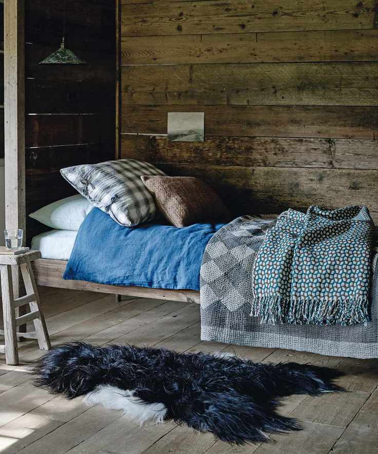 A cozy wood-panelled bedroom with a bed covered in blankets, and a black sheepskin rug on the floor