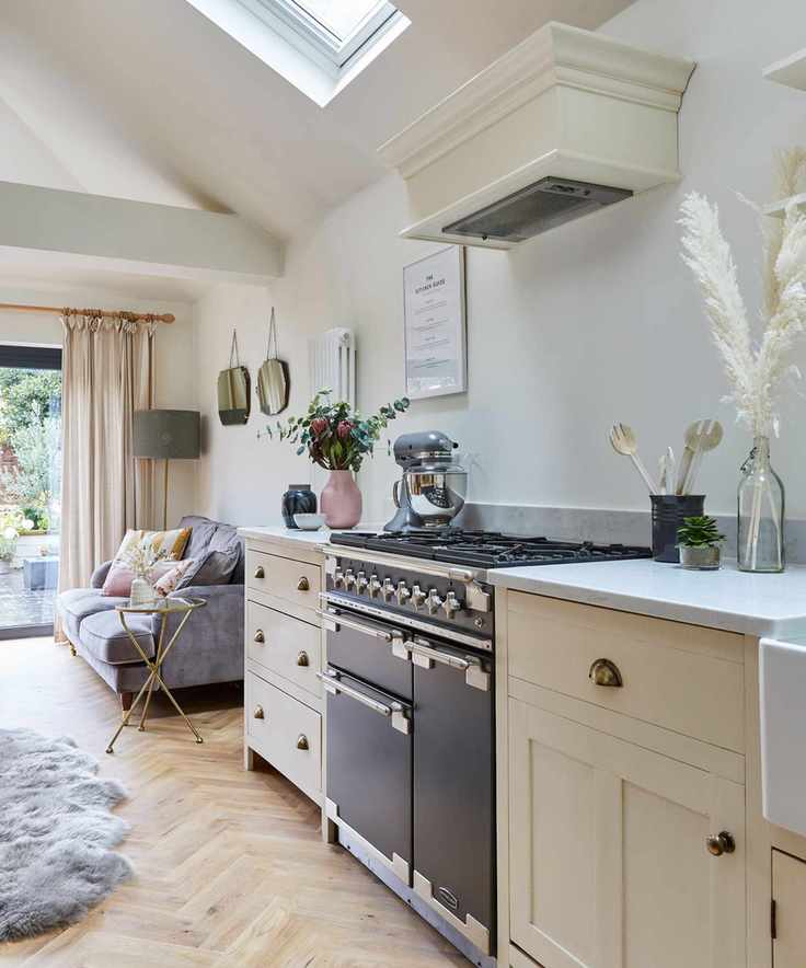 Neutral kitchen with cozy seating area beside window with curtains and sofa, light wood herringbone flooring