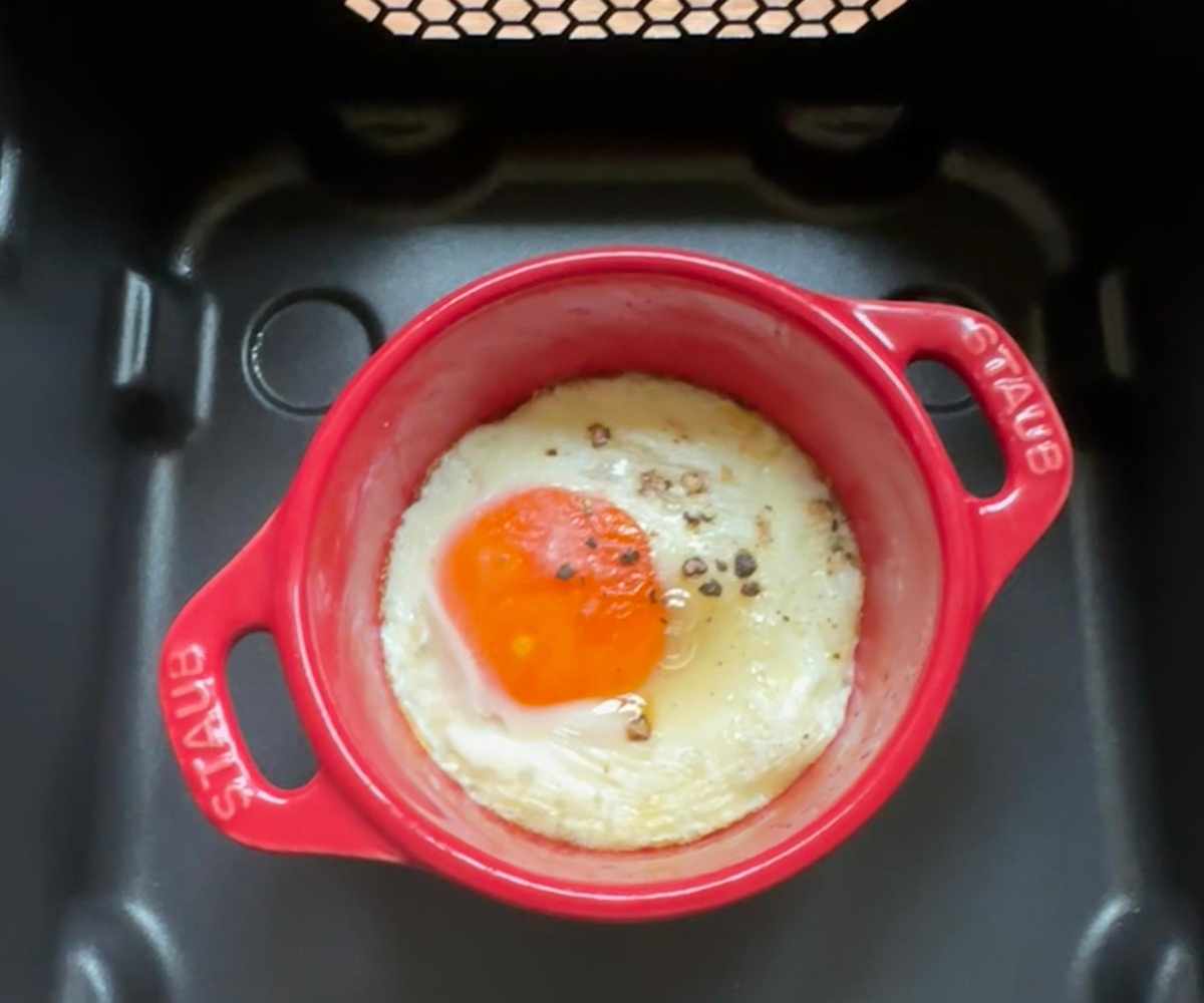 A small red STAUB ramekin inside a black air fryer basket, with a poached egg inside.