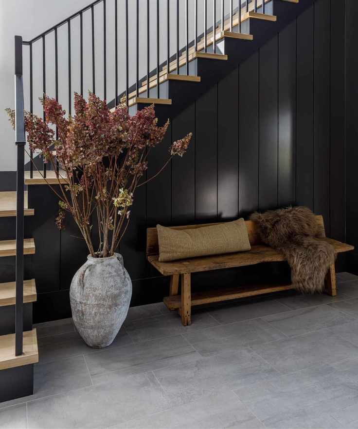 hallway with high gloss black panelling, contemporary iron railings, and a rustic wooden shoe bench with a cushion and furry throw