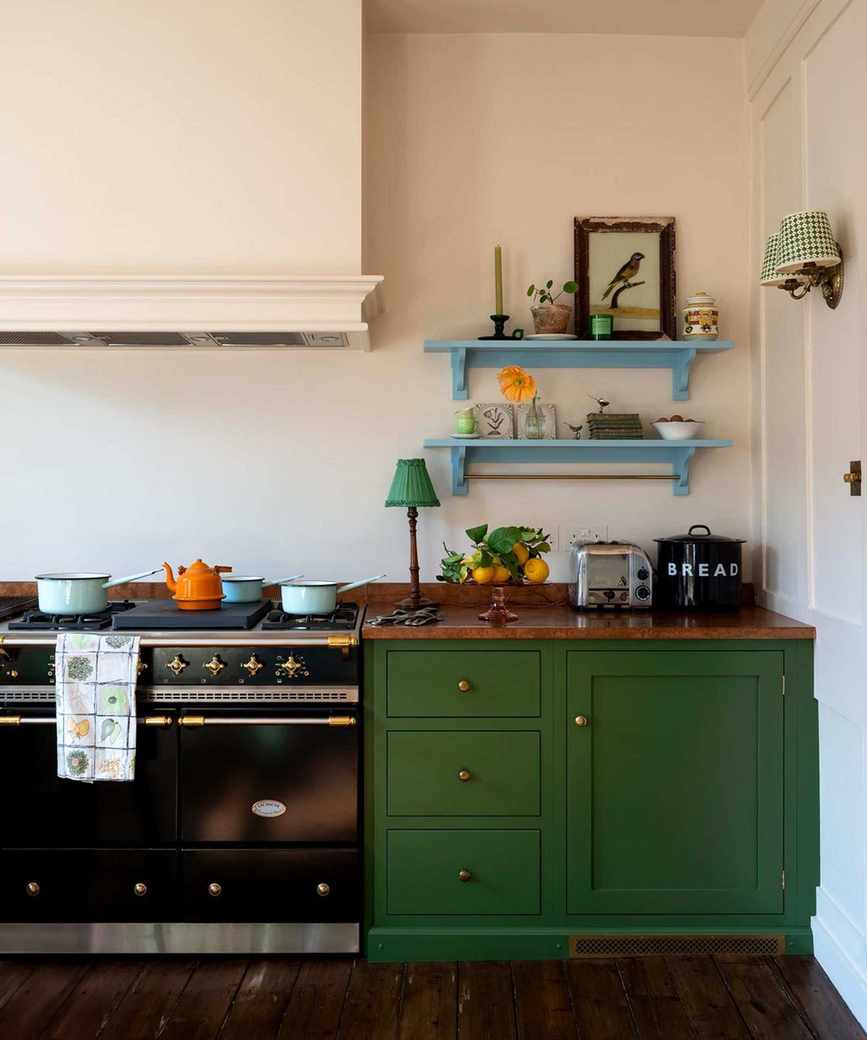 A small green kitchen with copper countertops and two blue floating shelves filled with vintage decor