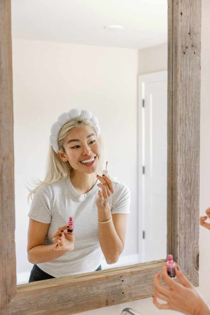 Woman applying lip gloss in mirror.