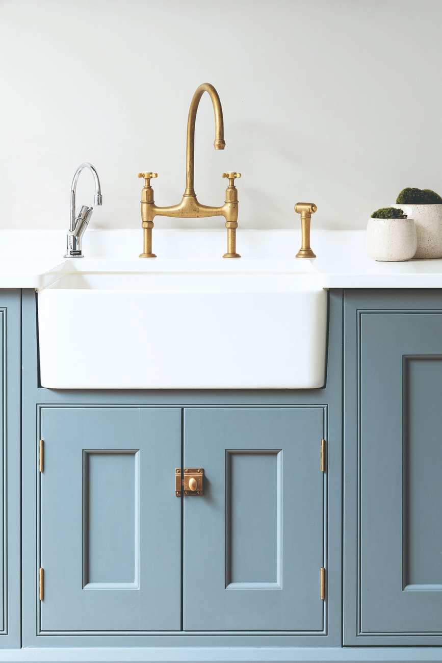 A white farmhouse sink above blue inlaid cabinets. Gold faucet.