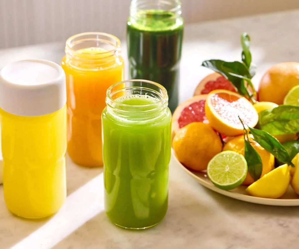 Four of Nama's single-serve glass bottles filled with juice, with a plate of citrus juice around it