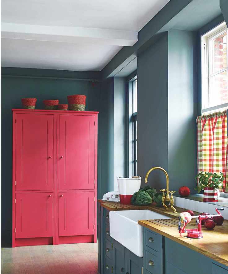 A stylish dark blue kitchen with pink cabinets and a wooden counter.