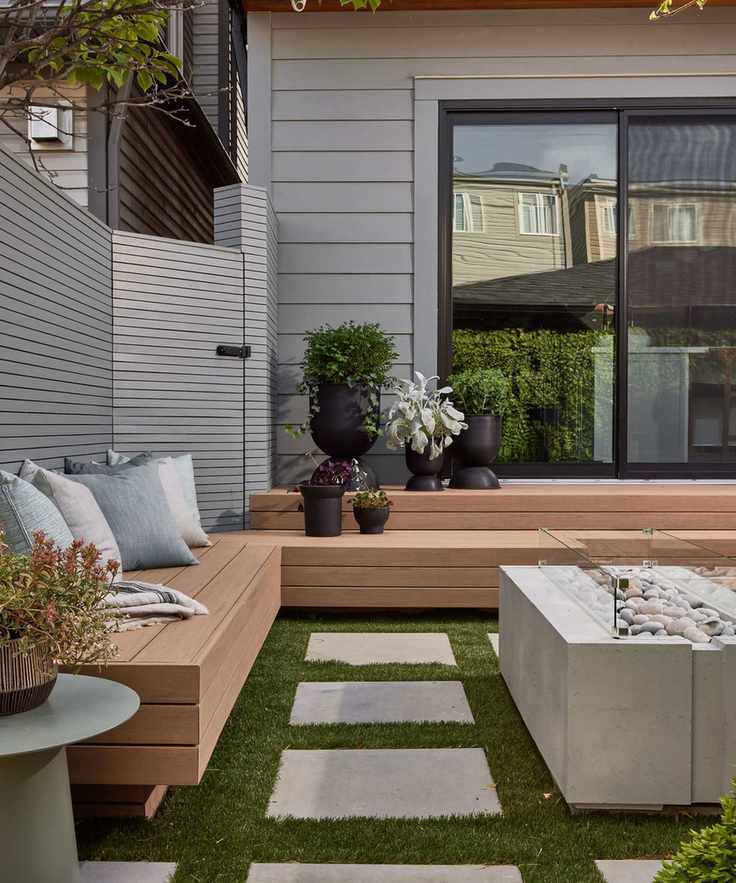 Wooden built-in bench in small backyard space with cushions and contemporary firepit