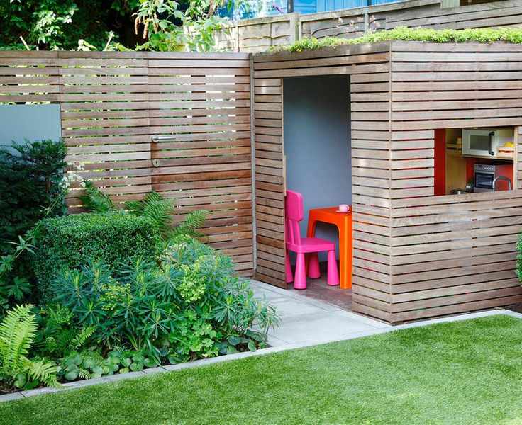 Concealed garden gate shown in a wooden slatted fence and gate combination, with square beds and lawn and a matching slatted garden room.