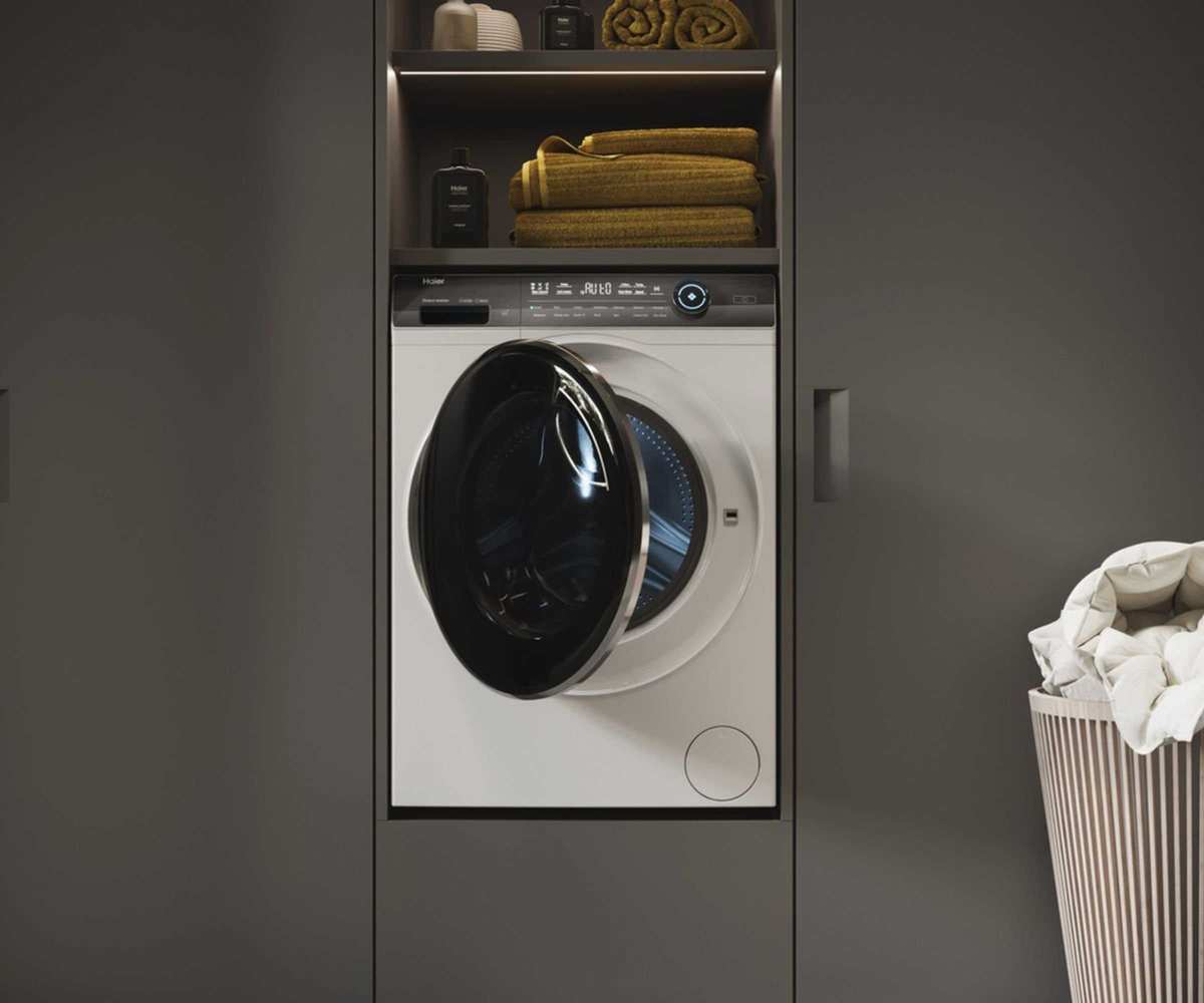 Integrated elevated white washing machine sitting in a wall of gray matte cabinets