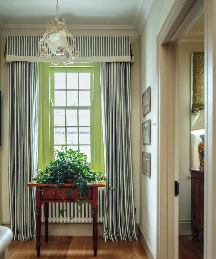 Green painted window with stripe curtains, wood table and art hanging on wall with metal chandelier