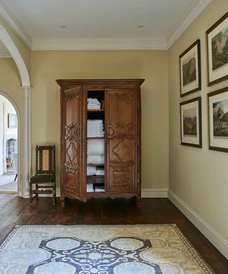 A brown linen closet in a hallway with a large patterned rug and framed gallery wall next to a wooden chair