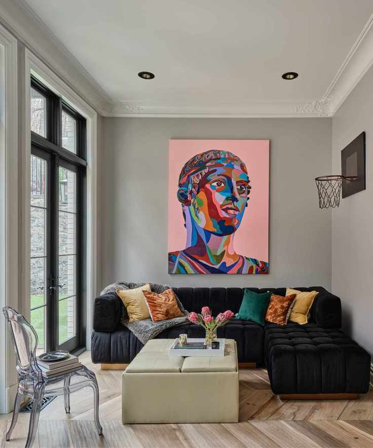 A living room with a black sectional, a beige ottoman, and a bright pink piece of art on the wall