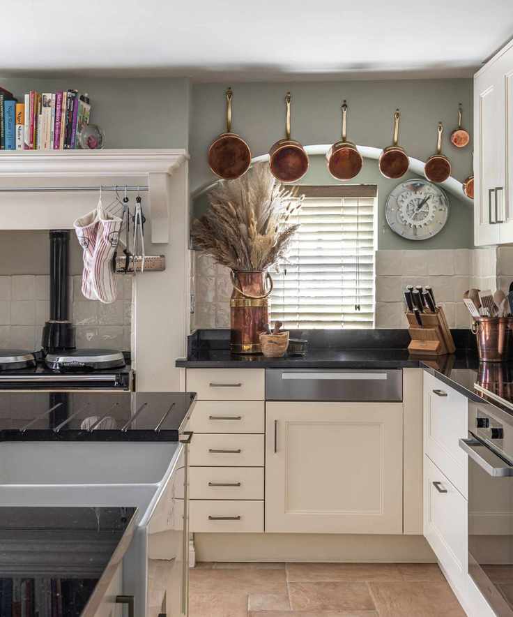 Country style kitchen with cream cabinets hooks above sink for hanging copper pots and tall shelving for cookbooks above range alcove