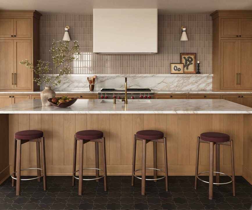 A wooden kitchen with marble countertops and a mixed material backsplash, which is half marble and half warm neutral tiles