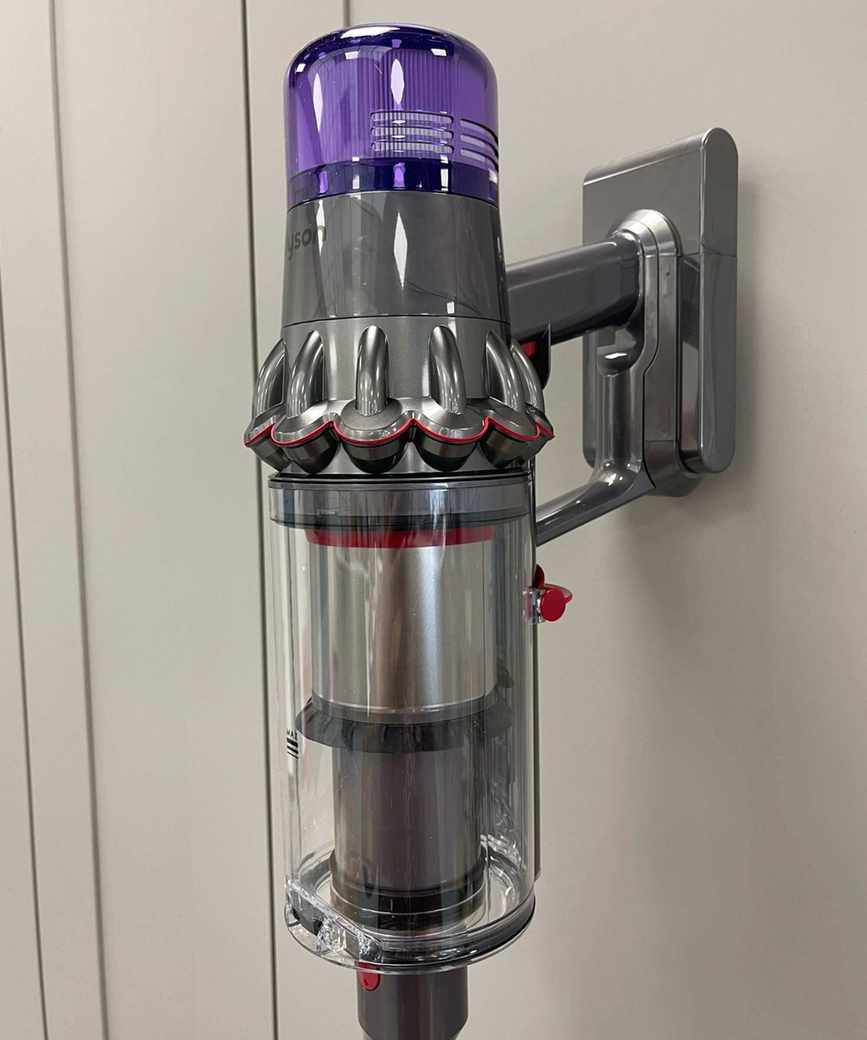 Dyson V11 cordless vacuum leaning on gray cabinet doors, in reflective gray and purple colorway.
