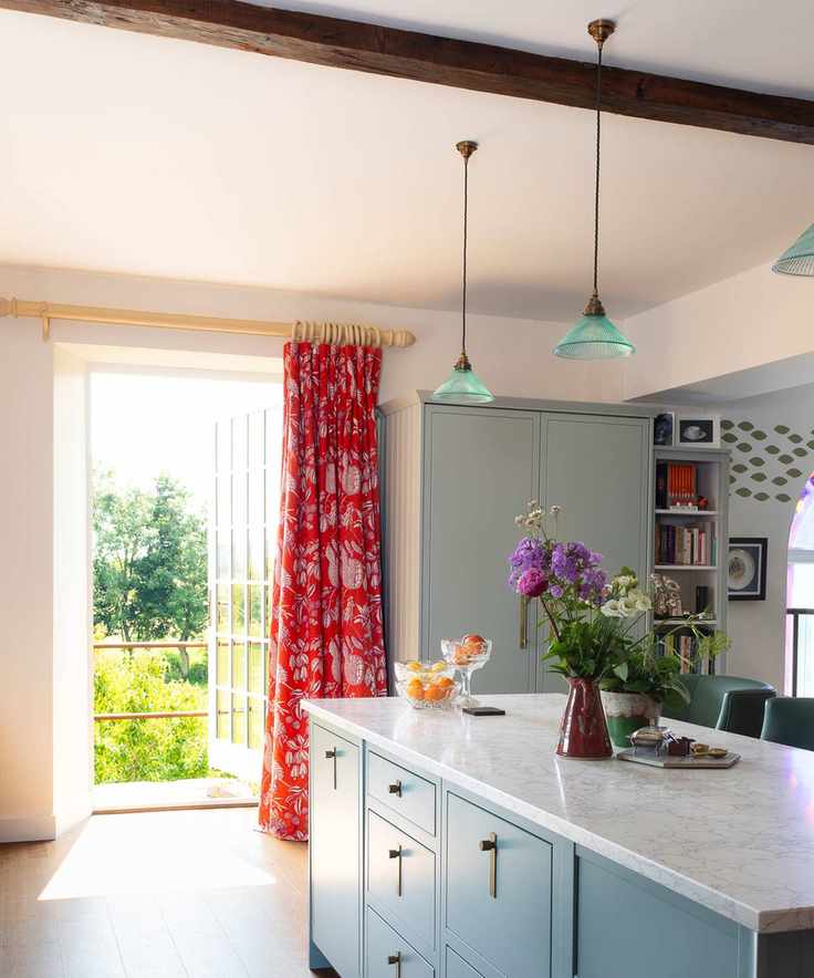 Country kitchen with blue kitchen island, matching cabinetry, blue glass pendant lights, red curtains