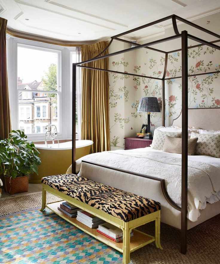 A vibrant room with a floral mural, a four-poster bed, and a stylish yellow bench at the foot